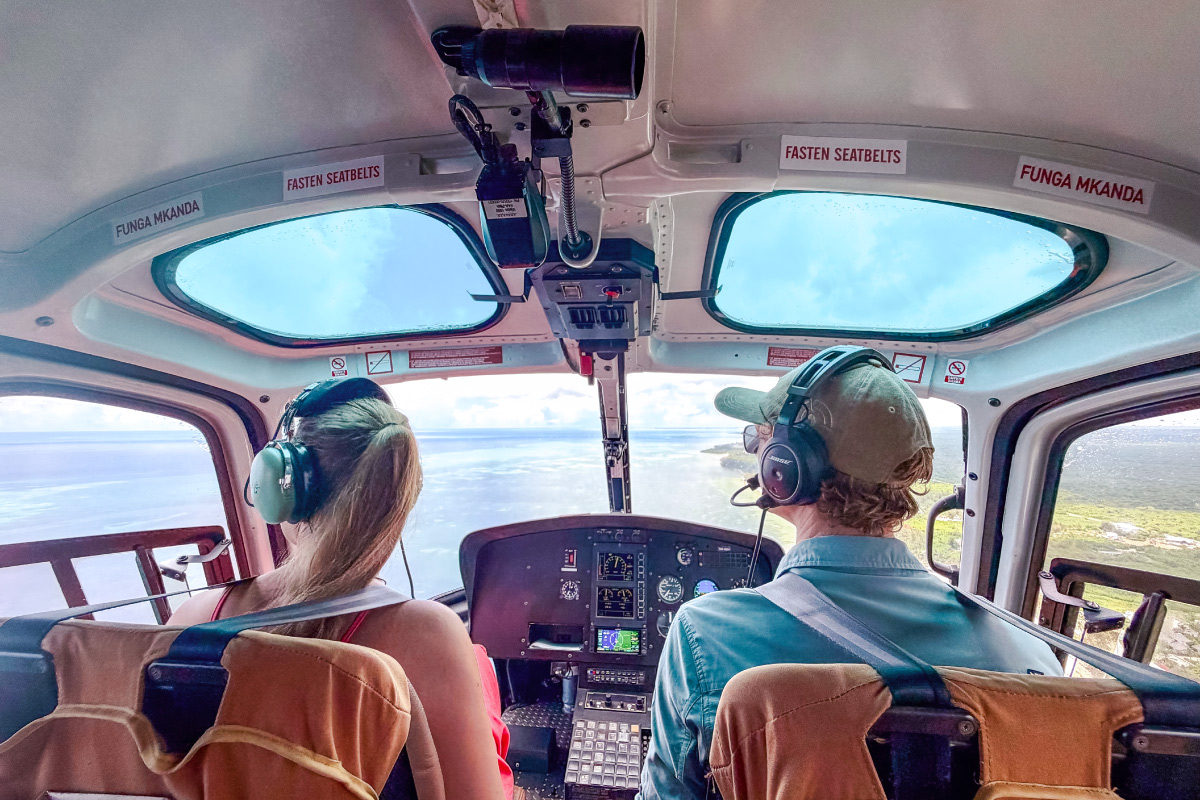 Two people are sitting in the cockpit of a helicopter, flying over Zanzibar