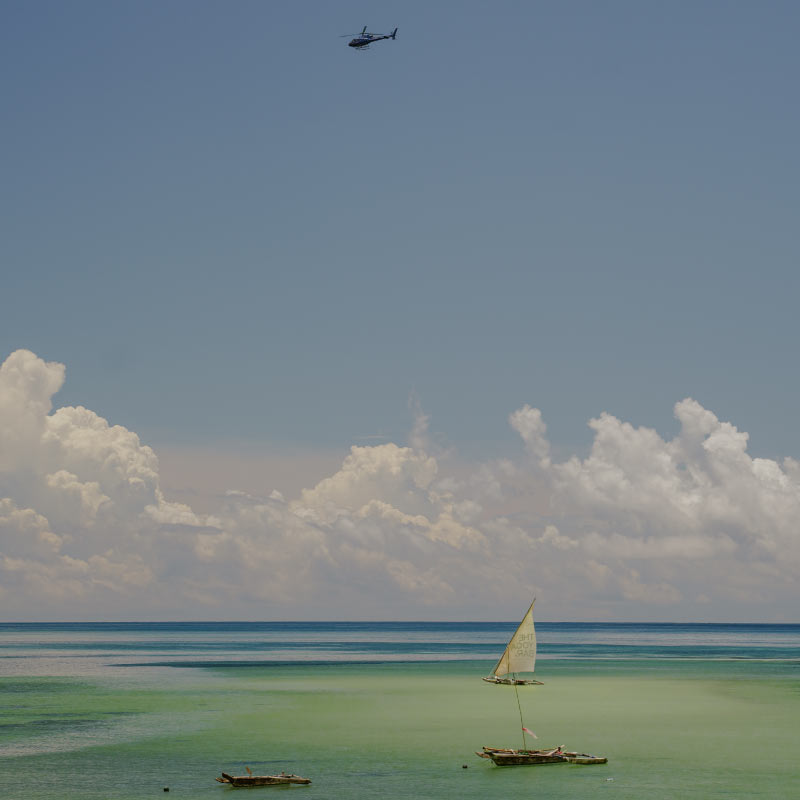 A helicopter is flying high in the sky above the sea